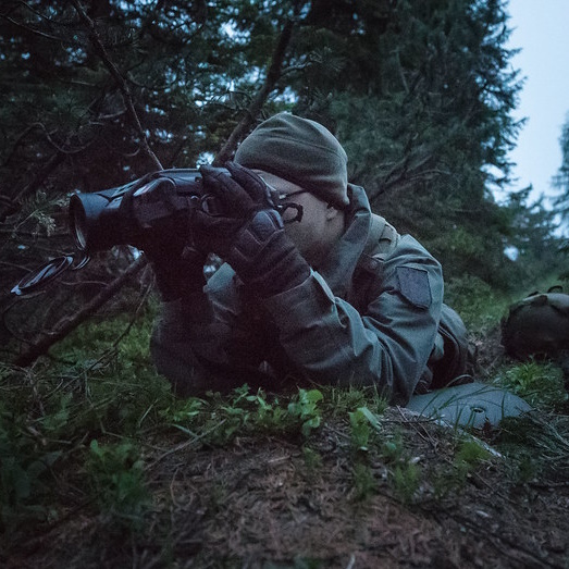 Unteroffizier der mit Nachtsicht-Gerät im Wald liegt